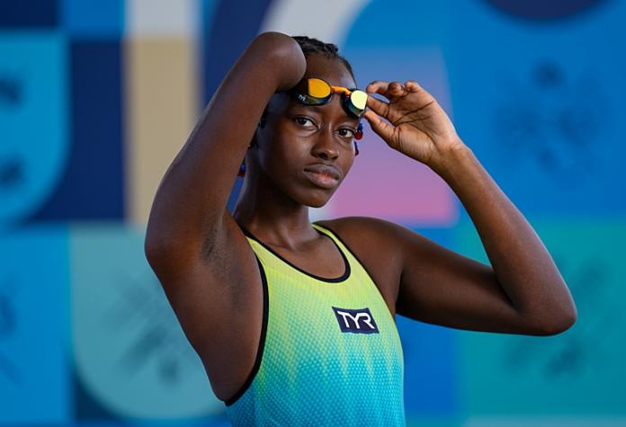 Husnah Kukudakwe, a female athlete from Uganda, is posing for a photo in her yellow and blue swimsuit. 