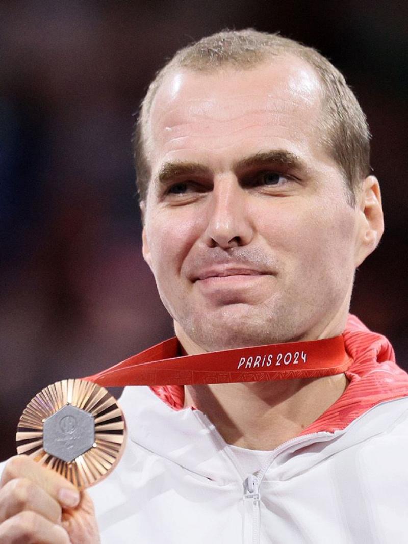 Michal Dabrowski is smiling while holding a bronze medal