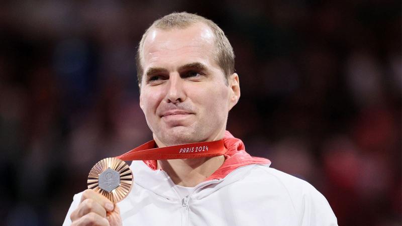 Michal Dabrowski is smiling while holding a bronze medal