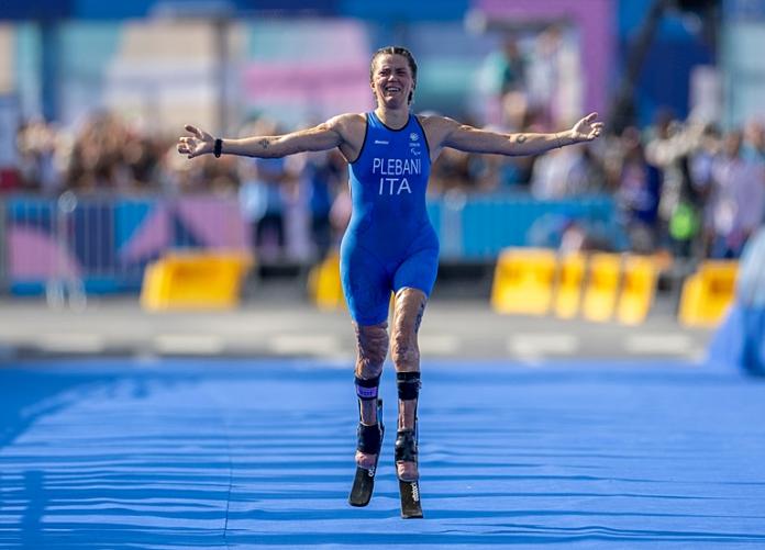 A female Para triathlete raises her arms during a race