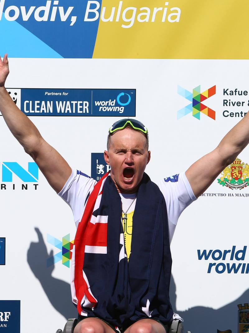 A man in a wheelchair celebrating in the middle of two men in wheelchair chairs clapping