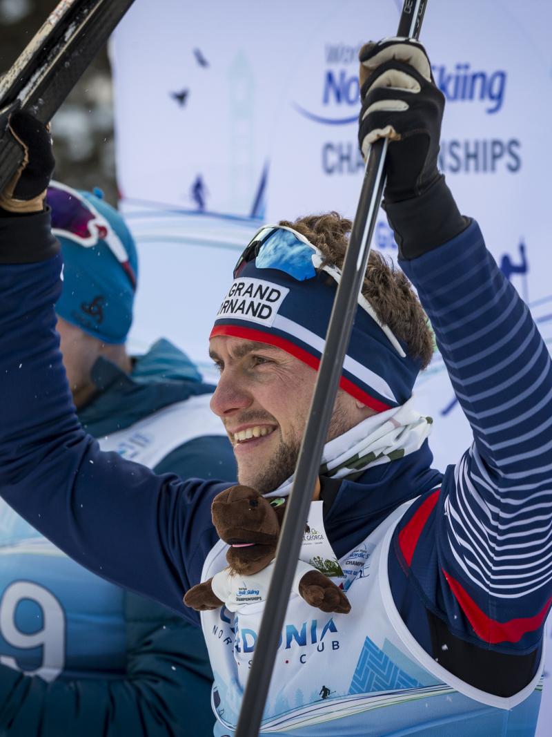 male Para Nordic skier Benjamin Daviet lifts up his skis in celebration on the podium