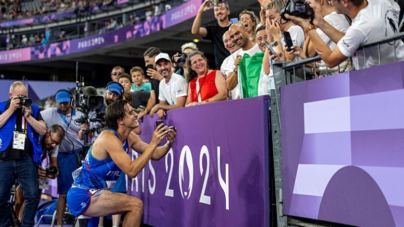 A man with a prosthetic leg kneeling to propose to his girlfriend in a packed stadium