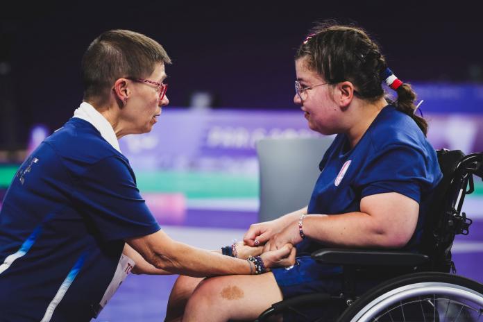 Boccia athlete Audrei Aubert and her coach Claudine Llop hold hands and face each other during competition