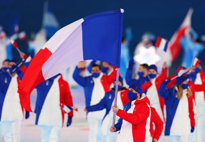 A male athlete wearing a face mask carries the French flag during the Opening Ceremony of Beijing 2022. He is wearing a blue, red and white uniform