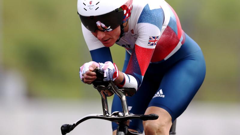 A woman in a Great Britain uniform and helmet rides a racing bicycle at Tokyo 2020.