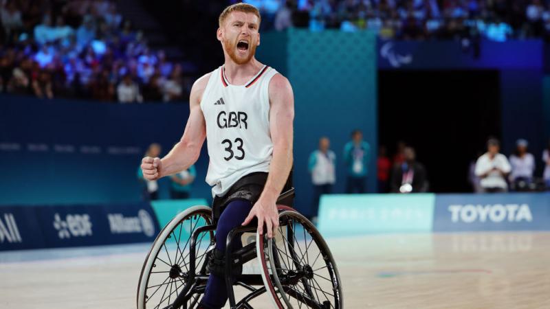 A man in a Great Britain uniform and a basketball wheelchair yells in celebration