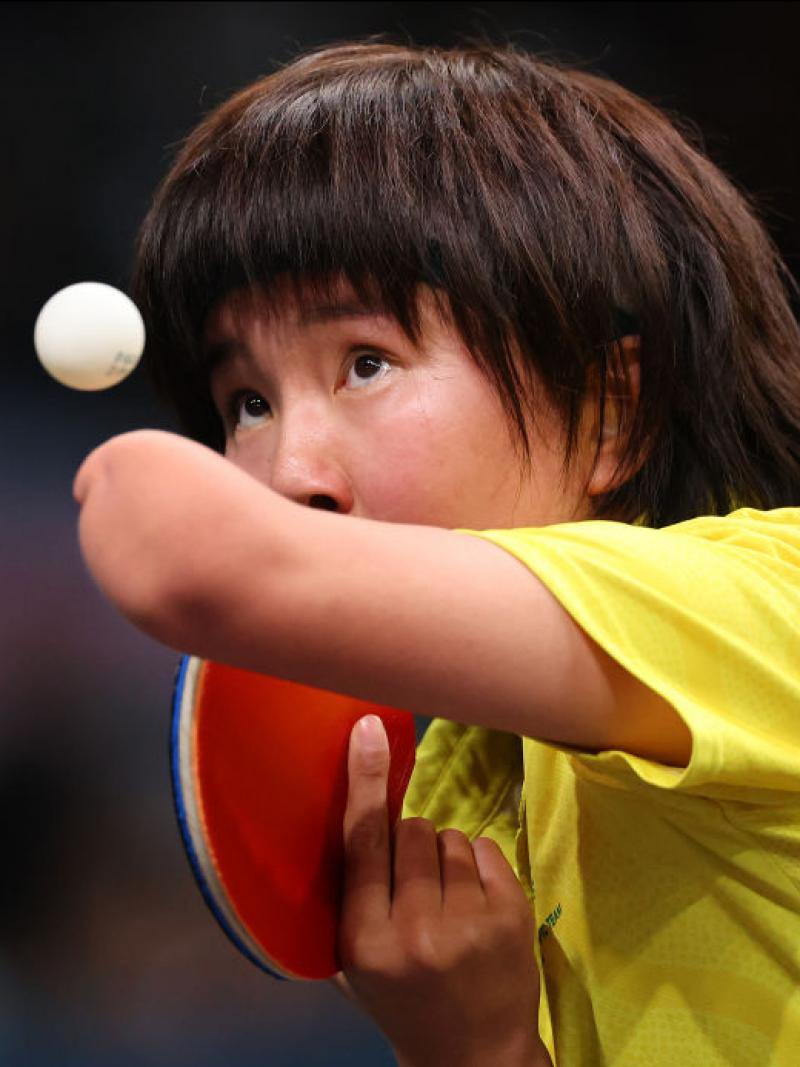 A table tennis player in a yellow shirt keeps her eye on the ball as she serves
