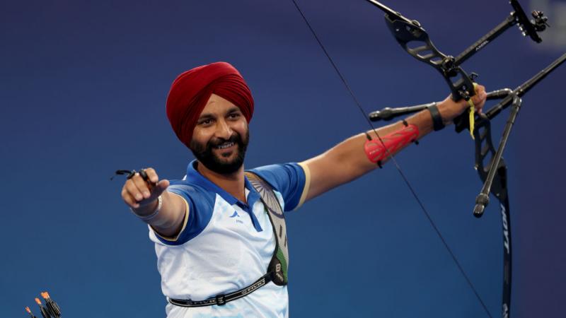 A man raises both arms in the air, carrying an archery bow in one hand
