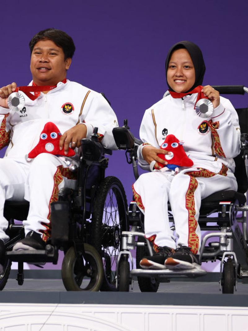 Three Indonesian boccia players in wheelchairs holding up their silver medals on the podium