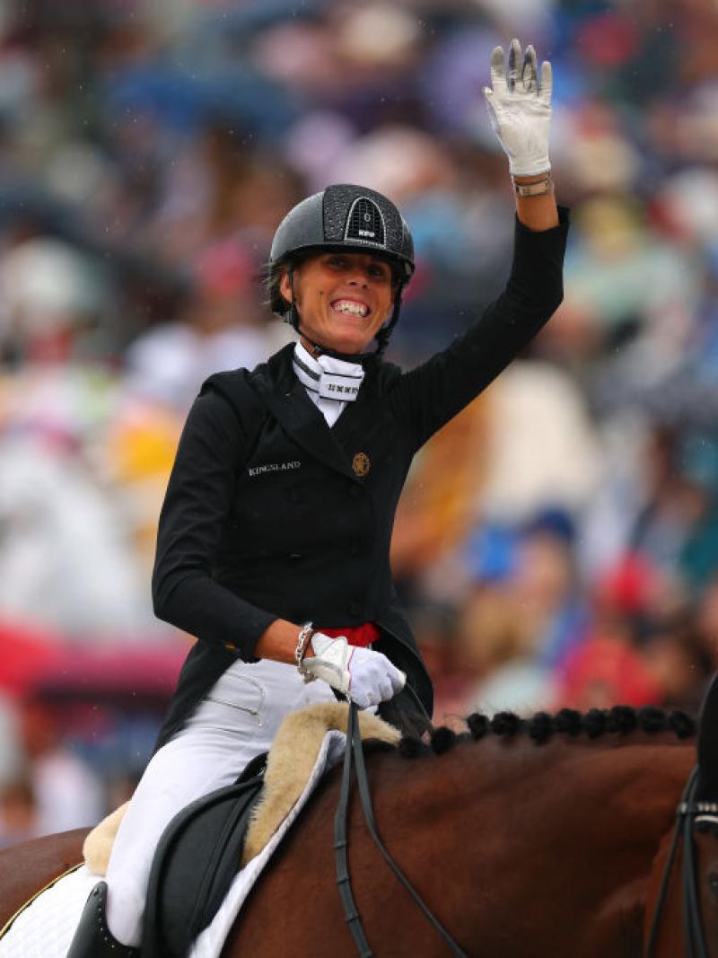 A female equestrian rider in a black jacket and helmet celebrates winning while sat on top of her horse