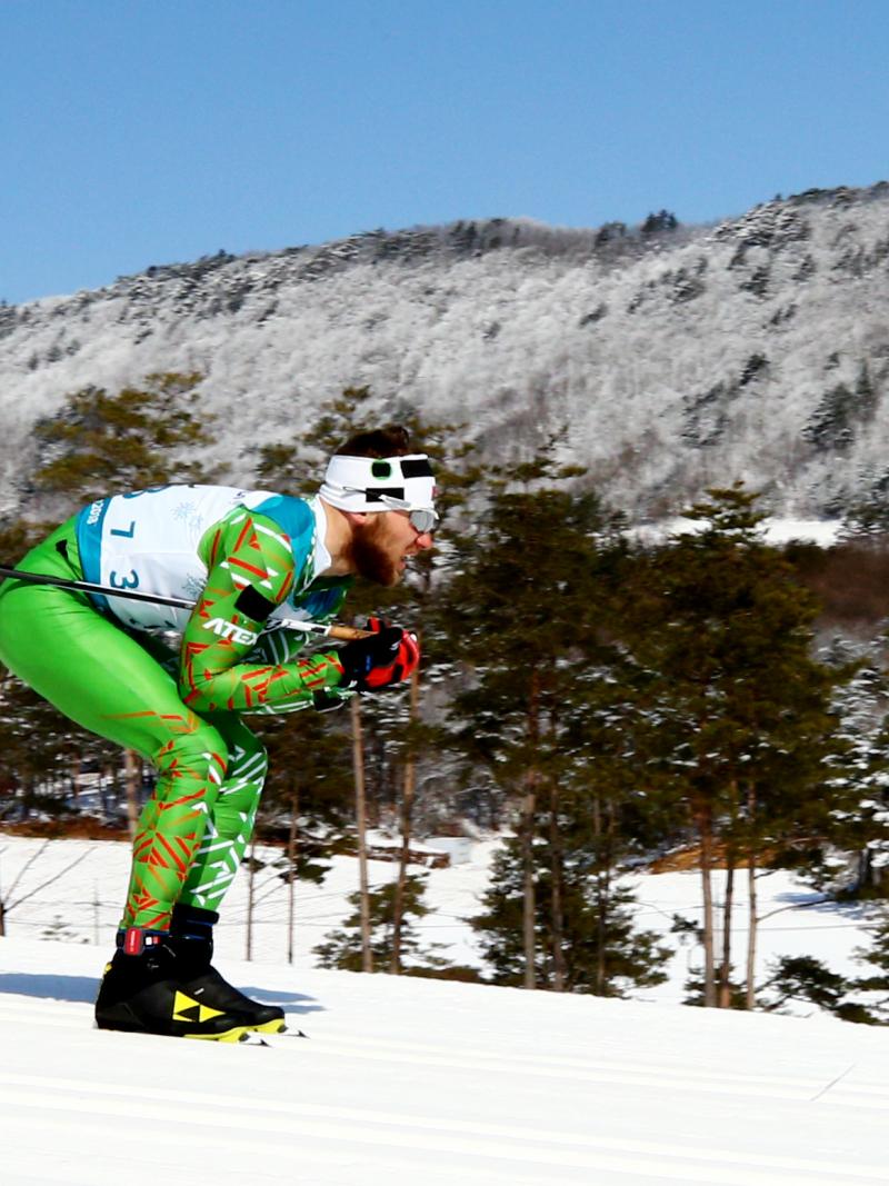 A man skiing wearing a green outfit and sunglasses