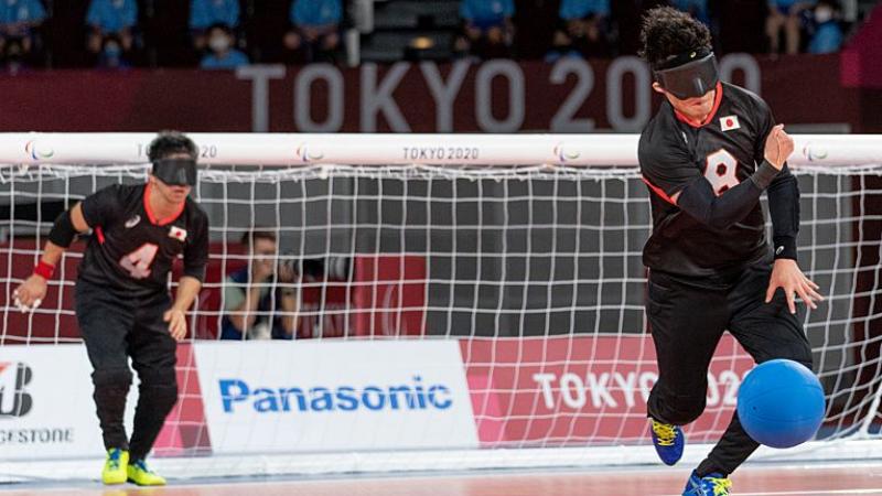 A male goalball player rolls the blue goalball in front of his net.