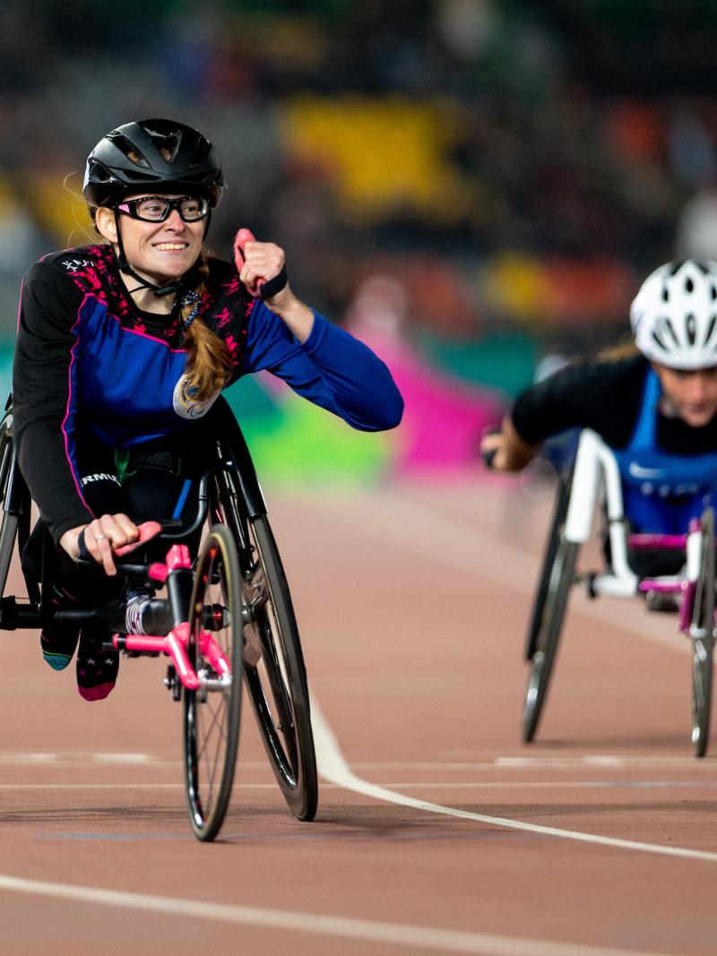 a female wheelchair racer clenches her fist as she crosses the finish line