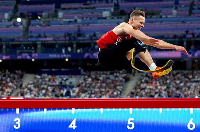 A male long jumper with a prosthetic running blade is competing in the long jump