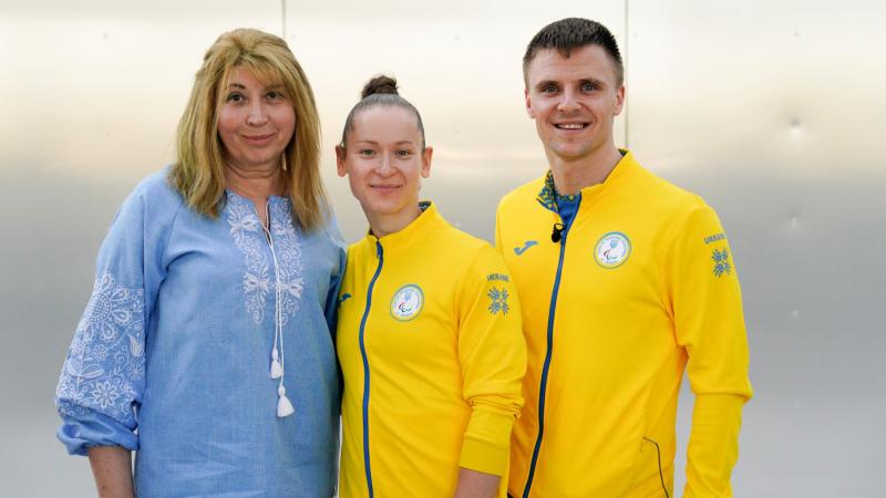 Oksana Kozyna and Oleksandr Chyrkov standing with their teacher and smiling 