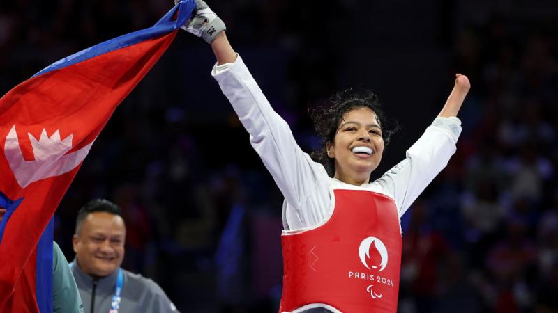 A female Para taekwondo athlete celebrates by holding Nepal's flag on the taekwondo mat