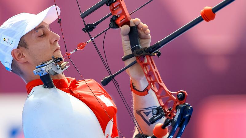 A man holds the bow with his legs and prepares to draw the arrow with his mouth.