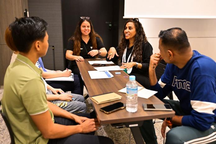 About five people are sitting around a desk to speak