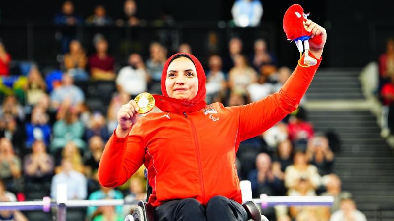 A woman in a wheelchair showing her medal to the public in an arena