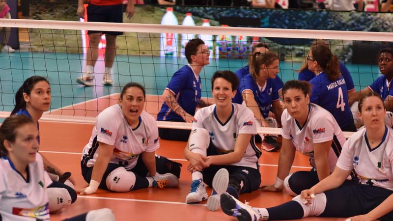Six female sitting volleyball players sitting on the court and smiling