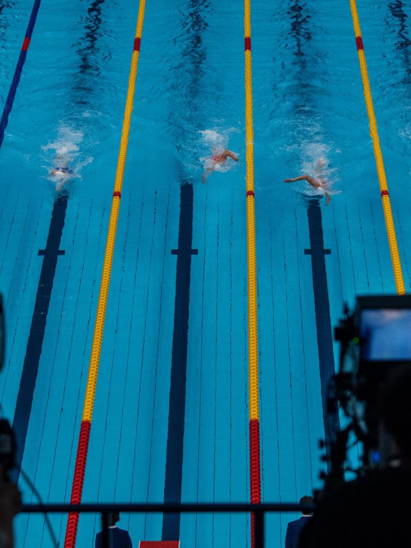 A look at a competition pool in Tokyo, with six swimmers in the lanes, through two cameras that are filming the race.